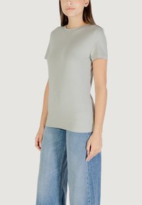 Maglietta a maniche corte grigia chiara con scollatura tonda. Il tessuto ha una texture liscia e presenta un design testuale discreto sul davanti.