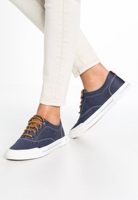 Marina kanvas sneakers med bruna snören och vita gummisulor. Funktioner inkluderar en rund tå, sömnadsdetaljer och en logotypaccents på sidan.