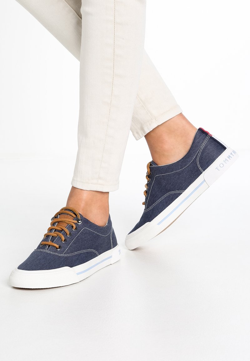 Marina kanvas sneakers med bruna snören och vita gummisulor. Funktioner inkluderar en rund tå, sömnadsdetaljer och en logotypaccents på sidan.