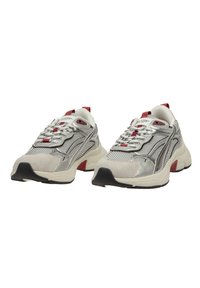 Zapatillas plateadas y beige con materiales de malla y ante. Presentan acentos rojos, suela gruesa y puntera redonda. Diseño con cordones y cuello acolchado.