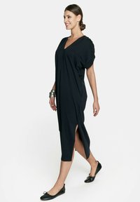 Czarna sukienka na ramiączkach z dekoltem w serek, krótkimi rękawami, asymetrycznym krojem i bocznymi rozcięciami. Noszona z płaskimi czarnymi butami i srebrnymi bransoletkami.