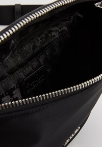 Interieur van een zwarte nylon tas met een ritsluiting, gladde voering met een subtiel patroon en een klein reliëflabel. Duurzaam en gestructureerd ontwerp.