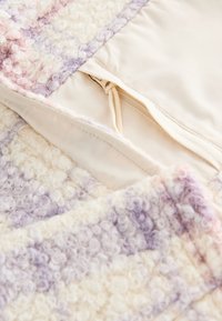 Nærbillede af en creme- og lavendelfarvet bouclejakke, der viser lynlåsområdet med stofbindedetalje og blødt tekstureret uldblandingsmateriale.