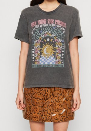 Maglietta grafica grigia con motivo di sole e fiori, abbinata a una minigonna arancione lucida con stampa effetto pelle di serpente.