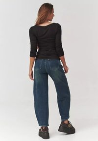 Czarny długi rękaw z dekoltem na plecach, w połączeniu z luźnymi niebieskimi dżinsami. Dżinsy mają wyblakły wygląd i tylne kieszenie.