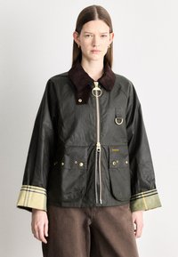 Must vahatatud jope pruunist sametkraega, kuldse luku ja taskutega. Varrukate mansettidel on ruuduline muster.