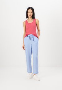Top sin mangas rojo con escote redondeado, combinado con unos pantalones sueltos de tono azul claro que tienen cintura elástica y cordón, complementados con unas zapatillas blancas.