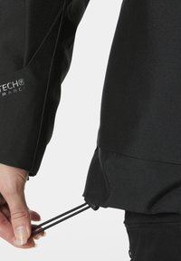 Černá bunda s důrazem na přesný střih u zápěstí s nastavitelnými šňůrkami a hladkým, texturovaným materiálem pro zvýšení výkonu.