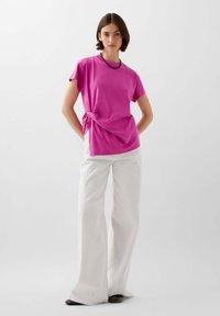 Fuchsia T-shirt met korte mouwen en een zij-knoopdetail, gecombineerd met witte wijde broek. Glad stoftextuur, minimalistisch ontwerp.