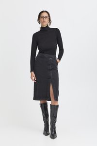 Haut à col roulé noir associé à une jupe en denim noir taille haute avec une fente à l'avant et des détails à boutons, complétés par des bottes noires montantes jusqu'aux genoux.