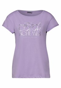 Lila t-paita lyhyillä hihoilla, jonka etupuolella on hopeinen teksti "luonnolliset VÄRISIHEET MAAPERÄNSÄVYJÄ" painettuna, pyöreä pääntie.