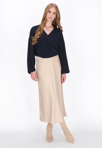 Mørkeblå bluse med V-hals og plisseringer, parret med en beige, ankellang, glat nederdel, suppleret af matchende figursyede beige støvler.
