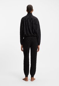 Sort sweatshirt- og bukse-sæt med et struktureret mønster. Sættet har en afslappet pasform med ribbede manchetter og krave.