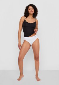 Zwarte cami met kanten rand, gecombineerd met witte onderkleding met een logo op de tailleband. Glad stof, aansluitend ontwerp.