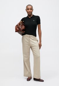 Zwarte geribbelde polo met een klein logo, beige wijde sweatpants en een bruine leren handtas met gouden hardwareaccenten.