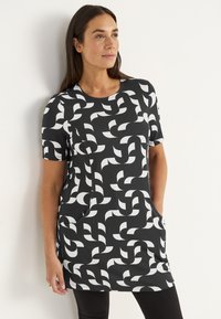 Korte mouwen tuniek in zwarte stof met een wit geometrisch patroon, ronde halslijn en zijzakken. Zachte textuur, casual pasvorm.