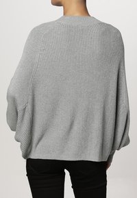 Světlé šedé oversize pletené svetr s kulatým výstřihem, spadlými rameny a žebrovanou strukturou. Zadní pohled, uvolněný střih.