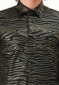 Schwarzes Shirt mit goldenen, wellenförmigen Linien auf dem Stoff. Es hat einen klassischen Kragen und eine geknöpfte Vorderseite. Glatte Textur.