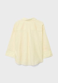 Chemise à manches longues jaune pâle vue de dos, avec un ourlet droit, de larges poignets et un col, sur un fond uni.