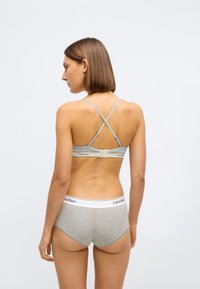 Bralette cinza com alças cruzadas, apresentando uma textura suave e fecho ajustável. Combinado com cuecas hipster cinza correspondentes com uma faixa branca.