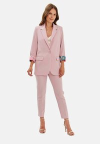 Jasnoróżowa marynarka z kolorowymi kwiatowymi akcentami na rękawach, w połączeniu z dopasowanymi spodniami i sandałkami na obcasie, z eleganckim krojem.