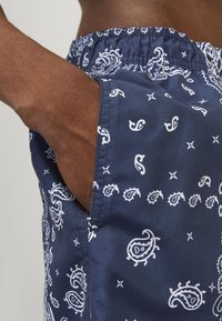Marinefarbene Schwimmshorts mit weißen Paisleymustern, elastischem Bund und seitlicher Tasche; aus glattem, leichtem Material gefertigt.
