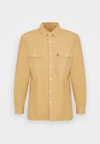 Chemise boutonnée couleur fauve en tissu léger, dotée d'un col, de deux poches poitrine et de boutons blancs. Coupe régulière avec manches longues.