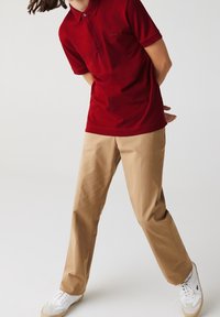 Polo rouge avec col, associé à un pantalon beige. Les baskets sont blanches avec des accents marron clair. Tissu lisse, coupe ajustée.