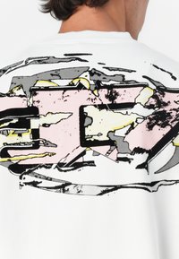 Sweatshirt branco com design gráfico abstrato em rosa, preto e cinza, com uma textura suave e decote canelado.