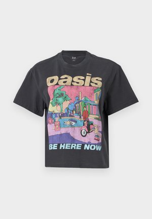 T-shirt en coton noir avec une coupe ample, présentant une impression graphique colorée d'une scène de rue, avec le texte "oasis" et "BE HERE NOW" en lettres majuscules.