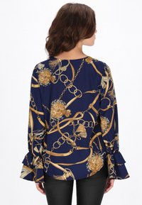 Tengerészkék blúz arany lánccal és virágmintával, bővülő ujjakkal és laza szabással, könnyű anyagból készült.