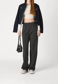 Chaqueta vaquera, top corto crema, pantalones anchos grises, bolso negro y zapatillas beige; características incluyen cintura elástica y pliegues laterales.