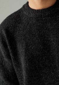 Maglione nero a maglia, con collo rotondo, in tessuto di lana testurizzato con un aspetto leggermente peloso. Presenta un colletto e dei polsini a coste.