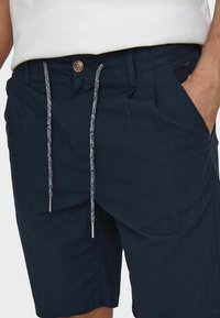 Pantaloni corti blu navy realizzati in tessuto texturizzato, caratterizzati da una chiusura con bottone, un cordoncino con punte in argento e tasche laterali.