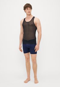 Fekete, áttetsző ujjatlan felső, testhez simuló fazonnal, tengerészkék boxer sorttal párosítva. A felső széles nyakkivágással és sima textúrával rendelkezik.