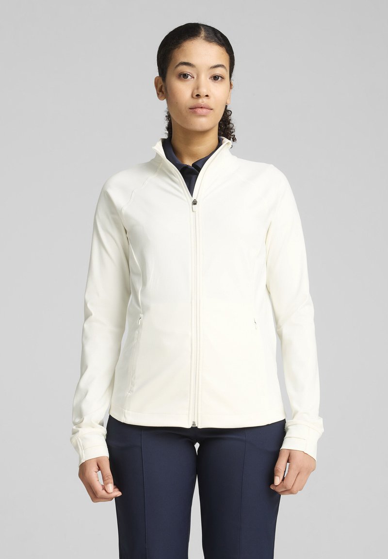 Veste zippée légère de couleur crème avec une coupe ajustée, texture douce et col montant. Comprend des poches latérales et des poignets texturés.