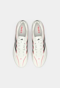 Weiße Fußballschuhe mit schwarzen und roten Akzenten, ausgestattet mit einem glatten Synthetik-Obermaterial, runder Zehenpartie und flachen Schnürsenkeln. Markenlogo sichtbar.