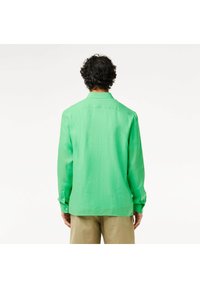 Camicia a maniche lunghe in lino verde brillante. Caratterizzata da un colletto classico e polsini con bottoni, con una vestibilità comoda e un dettaglio sulla spalla posteriore.