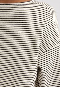 Knitted sweater in cream with narrow black stripes. Features a wide neckline and textured fabric. Styled with a loose fit and soft feel.