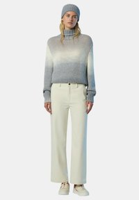 Maglione a maglia grigio con collo alto, abbinato a pantaloni larghi crema e sneakers bianche con accenti rossi. Dettagli del tessuto strutturato visibili.