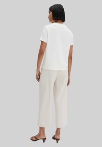 White short-sleeve top made of textured fabric, paired with light beige wide-leg pants. Brown heeled sandals complete the outfit.