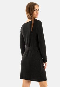 Abito lungo nero a maniche lunghe realizzato in tessuto testurizzato, con vita cintrata e tasche laterali, caratterizzato da un delicato luccichio generale.