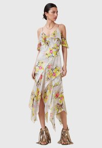Floral maxi-jurk van doorzichtig materiaal, met gele en roze bloemen, gerimpelde mouwen en een high-low zoom. Gecombineerd met metallic franje sandaaltjes.