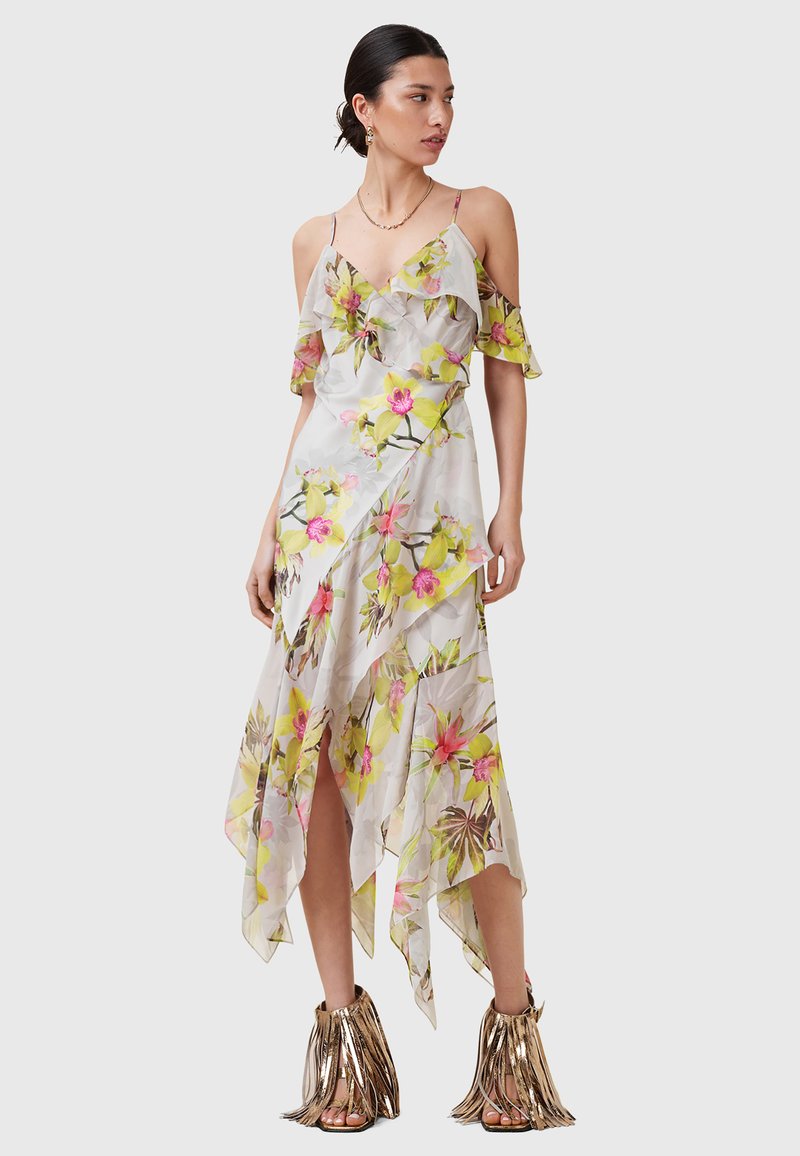 Floral maxi-jurk van doorzichtig materiaal, met gele en roze bloemen, gerimpelde mouwen en een high-low zoom. Gecombineerd met metallic franje sandaaltjes.