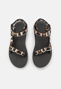 Sandalias negras con suelas texturizadas y tiras de tela con patrón en colores naranja, crema y negro. Cintas ajustables en el tobillo y en la parte delantera del pie.