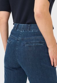 Donkerblauwe spijkerbroek van denim met een middenhoogte taille, rechte pijpen en twee achterzakken. Heeft een gestructureerde tailleband en minimale stikseldetails.