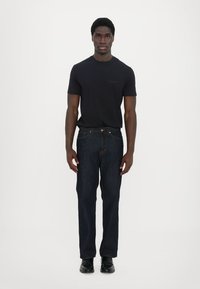 Marineblå kortermet t-skjorte kombinert med mørke denim jeans. Mannen står rett med svarte lær sko. Enkel, klassisk design.