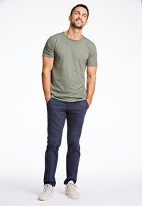 Olivgrünes Rundhals-T-Shirt, marineblaue Hose und weiße Sneakers. Das T-Shirt ist figurbetont, hat kurze Ärmel und eine glatte Textur.