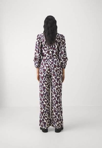 Printed jumpsuit featuring long sleeves, wide legs, in white with abstract maroon and blue patterns, with a fitted waistline and ruffled cuffs.