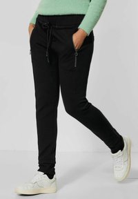 Svarta joggarbyxor med en strukturerad yta, med dragsko i midjan och två zip-fickor på sidorna, kombinerade med vita sneakers.